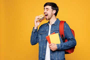 Young happy boy student he wearing denim casual clothes backpack bag holding books eat fast food...