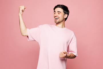Young excited Caucasian man he wearing t-shirt casual clothes doing winner gesture celebrate clenching fists say yes isolated on plain pastel light pink background studio portrait. Lifestyle concept.