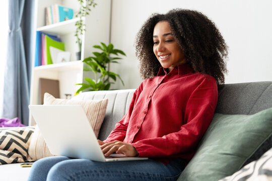 Smiling African American freelancer working from home using laptop on sofa