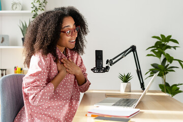 Excited young African American woman recording podcast from her home studio