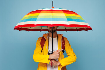 Traveler man wear hat yellow raincoat casual clothes hold umbrella point aside isolated on plain...