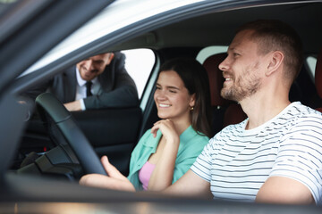Salesman showing new car to happy family, selective focus