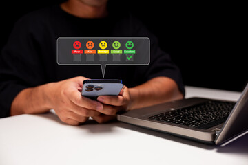 A person uses a smartphone near a laptop, interacting with an online feedback emoji rating system...