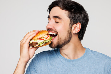 Close up young European man he wear blue t-shirt casual clothes hold eat bite burger with closed...