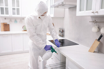 Pest control worker in protective suit spraying insecticide at home