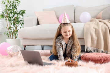 Birthday celebration. Little girl with cake having video call via laptop at home