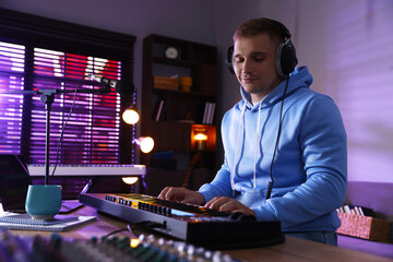 Man in headphones working with MIDI keyboard at table in home studio, low angle view