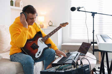 Man in headphones working with MIDI keyboard and guitar at table in home studio