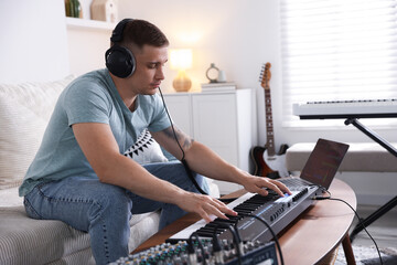 Man in headphones working with MIDI keyboard at table indoors