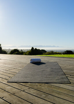 Dark gray yoga mat lying flat on deck, topped with rolled towel, overlooking misty mountain valley