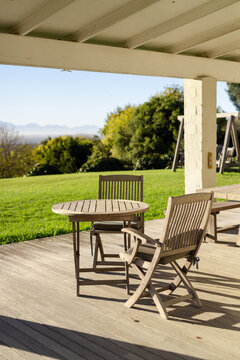 Round wooden table and two folding chairs resting on deck under white patio roof, mountain backdrop