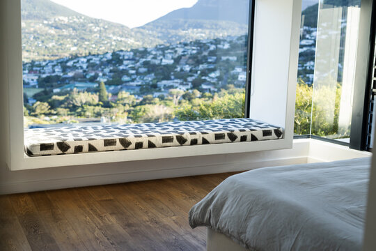 Built-in window seat cushion resting on bedroom wooden floor beside bed under large picture window