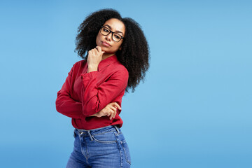 Pensive young woman touching chin and looking away on blue background