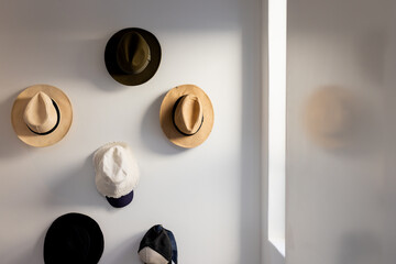 Six hats creating simple grid display on white wall in home hallway, with soft daylight