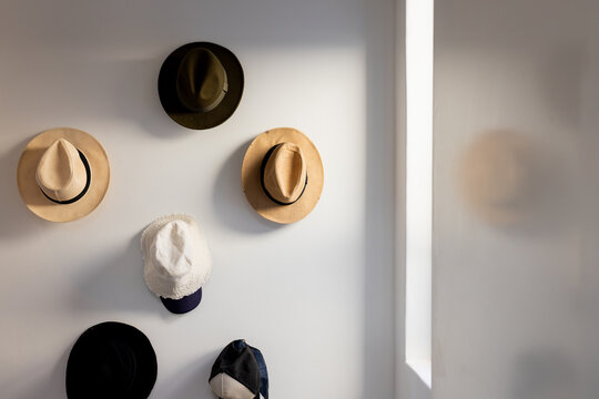 Six hats creating simple grid display on white wall in home hallway, with soft daylight