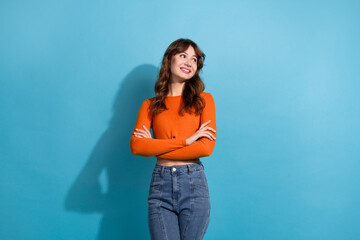 Young woman in a trendy orange top and jeans posing confidently in front of a bright blue...