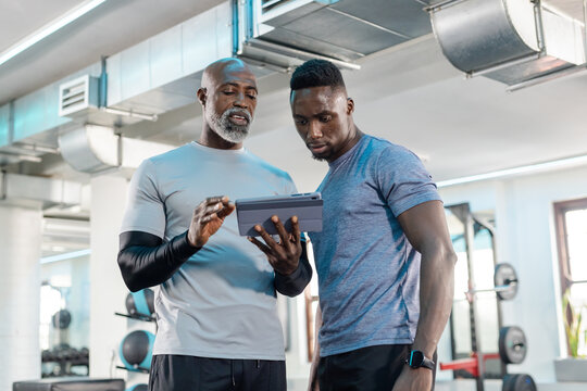 African American men studying workout data on tablet at fitness center with dumbbell rack and bench