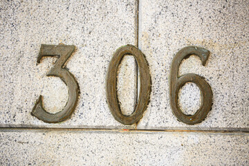 House number 306 in aged bronze mounted on a speckled granite wall. The oxidized metal digits...