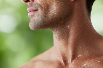 Naklejka premium Close up of man jawline and neck covered with water droplets, showing smooth skin texture and fresh, hydrated appearance against blurred green background