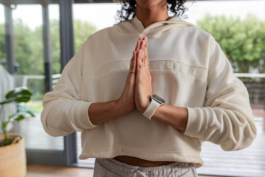 Non-binary person standing at home near glass doors pressing palms with smartwatch and potted plant