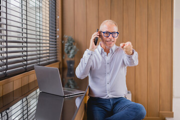 Senior businessman sitting at his desk in a modern office. Talking on the phone and pointing...