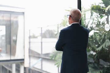 Mature business executive stands by a window, arms crossed, contemplating future opportunities. The...