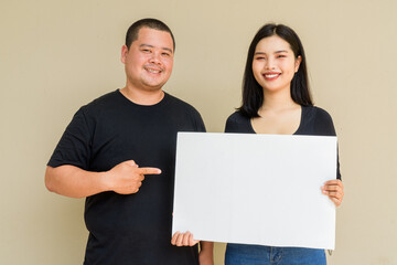 Portrait of young couple against plain wall background holding placard with copy space