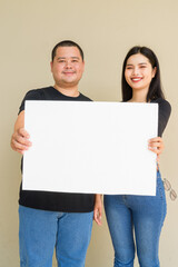 Portrait of young couple against plain wall background holding placard with copy space