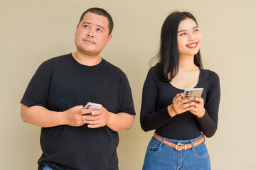 Portrait of young couple against plain wall background using phone