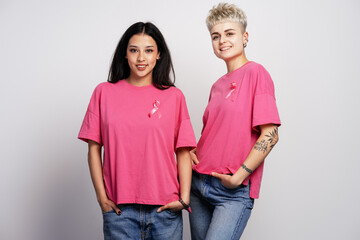 Two young women wearing pink ribbons for breast cancer awareness posing with hands in pockets