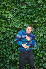 Man suffering heart attack clutching chest and abdomen standing against ivy wall