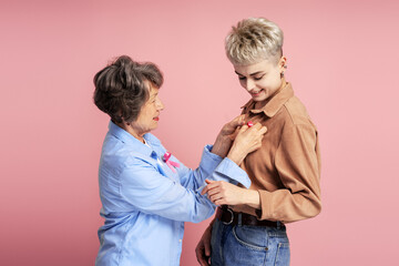 Senior woman pinning pink ribbon on young woman for breast cancer awareness