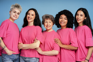 Five diverse women wearing pink t shirts are smiling and posing together