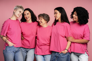 Five diverse women wearing pink t shirts are smiling and embracing, promoting breast cancer awareness