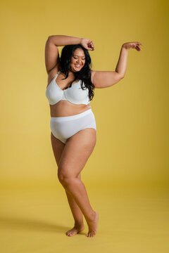 Woman posing gracefully in white bra and underwear on yellow studio floor, smiling and dancing