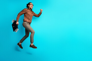 Confident businessman leaps with briefcase against vibrant teal background, embracing success and...
