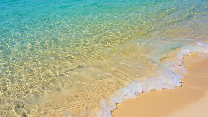 Crystal clear turquoise water gently washes over the golden sand creating a serene beach scene.