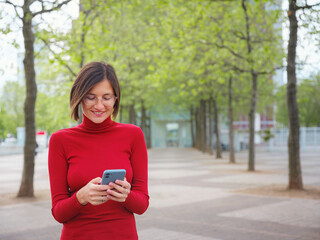 Beautiful woman in walking in Frankfurt on spring day and holding mobile phone. Urban lifestyle...