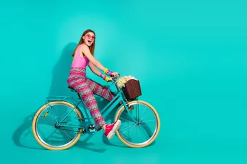 Fotobehang Young girl riding a teal bicycle against a turquoise background showcasing vibrant summer fashion with retro accessories © deagreez