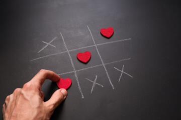 Hand placing final heart in winning tic-tac-toe line drawn with chalk.