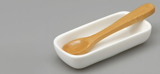 Wooden spoon resting on a white ceramic dish against a neutral gray background, showcasing the elegant design and functionality of kitchen utensils for culinary use