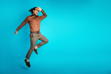 Energetic young businessman in brown attire making a joyful leap against a teal background...