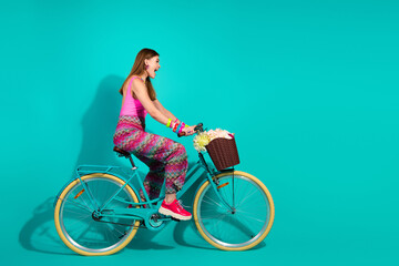 Young woman riding a retro bicycle with a flower-filled basket against a bright turquoise background