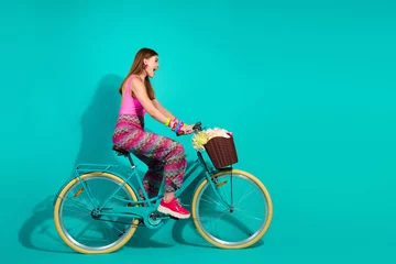 Fotobehang Young woman riding a retro bicycle with a flower-filled basket against a bright turquoise background © deagreez