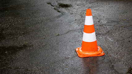 Traffic cone marking a wet asphalt road after a rain, warning drivers and pedestrians in a busy...