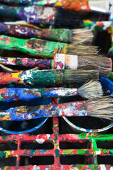 Fototapeta premium Concept of art, painting, and color: authentically paint-covered brushes on a paint-smeared drying rack for art tools in a studio or creative space, lived creativity, visible signs of real use