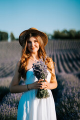 Young woman in a white dress holds lavender bouquet in a field during sunset