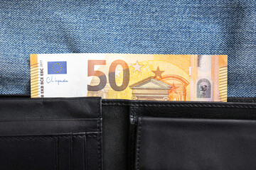 Fifty euro banknote sticking out from leather wallet. Closeup on money and denim background....