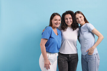 Fototapeta premium Three friends hugging on light blue background, space for text