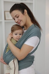 Mother holding her child in sling (baby carrier) at home